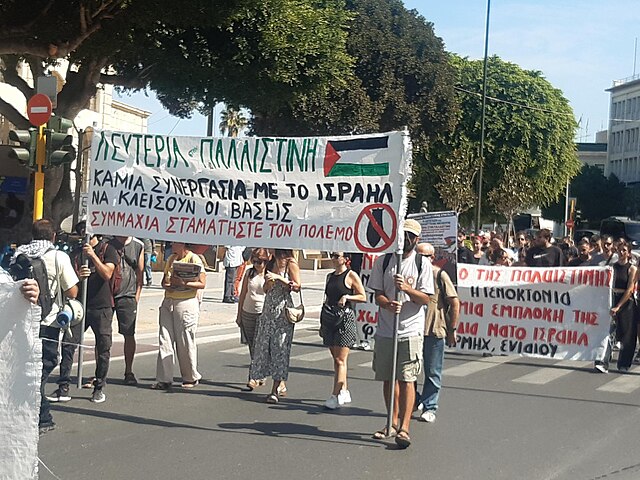 Pro-Palestinian demonstrators in Greece hold banners and flags during an anti-Israel protest in a city street.