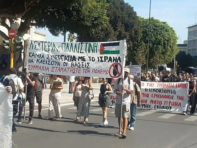 Pro-Palestinian demonstrators in Greece hold banners and flags during an anti-Israel protest in a city street.