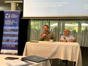 Sacha Roytman and Natan Sharansky speak into microphones during a fireside chat at the CAM Partners Roundtable Forum in Tel Aviv, seated at a table in front of a screen and CAM banner.