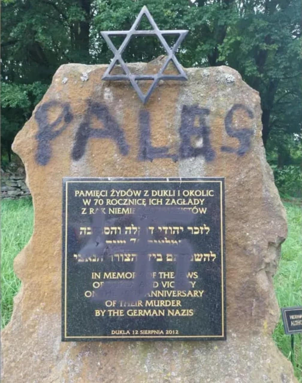 Stone Holocaust memorial in Dukla, Poland, defaced with spray-painted word “Palestine” beneath a Star of David, obscuring a plaque commemorating the town’s Jewish victims of the Holocaust.