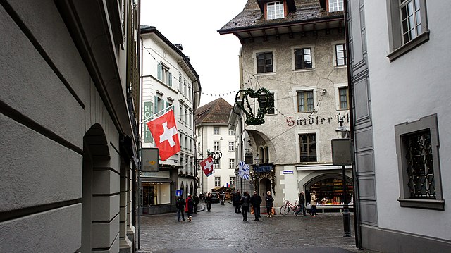 Historic street in Lucerne, Switzerland, with Swiss flags and pedestrians