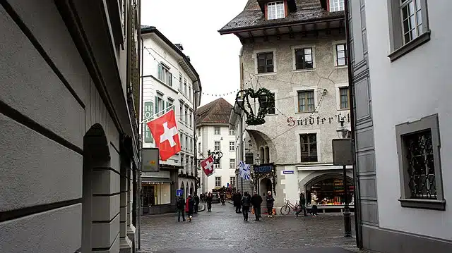 Historic street in Lucerne, Switzerland, with Swiss flags and pedestrians