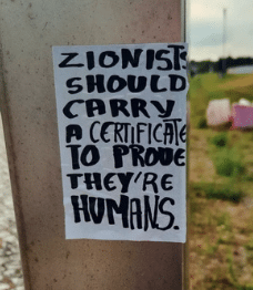 Sticker on a metal pole with handwritten text reading “Zionists should carry a certificate to prove they’re humans,” displayed in Coimbra.