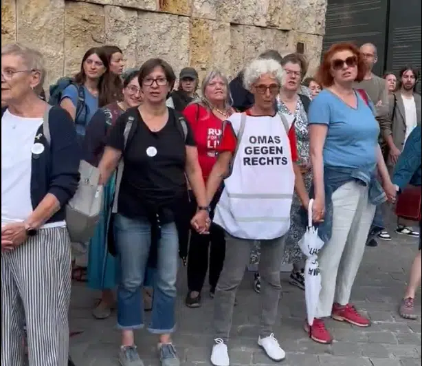 A diverse group of citizens stands hand in hand outside the Jakob Synagogue in Munich, forming a human chain of solidarity to shield it from a nearby pro-Palestinian protest.