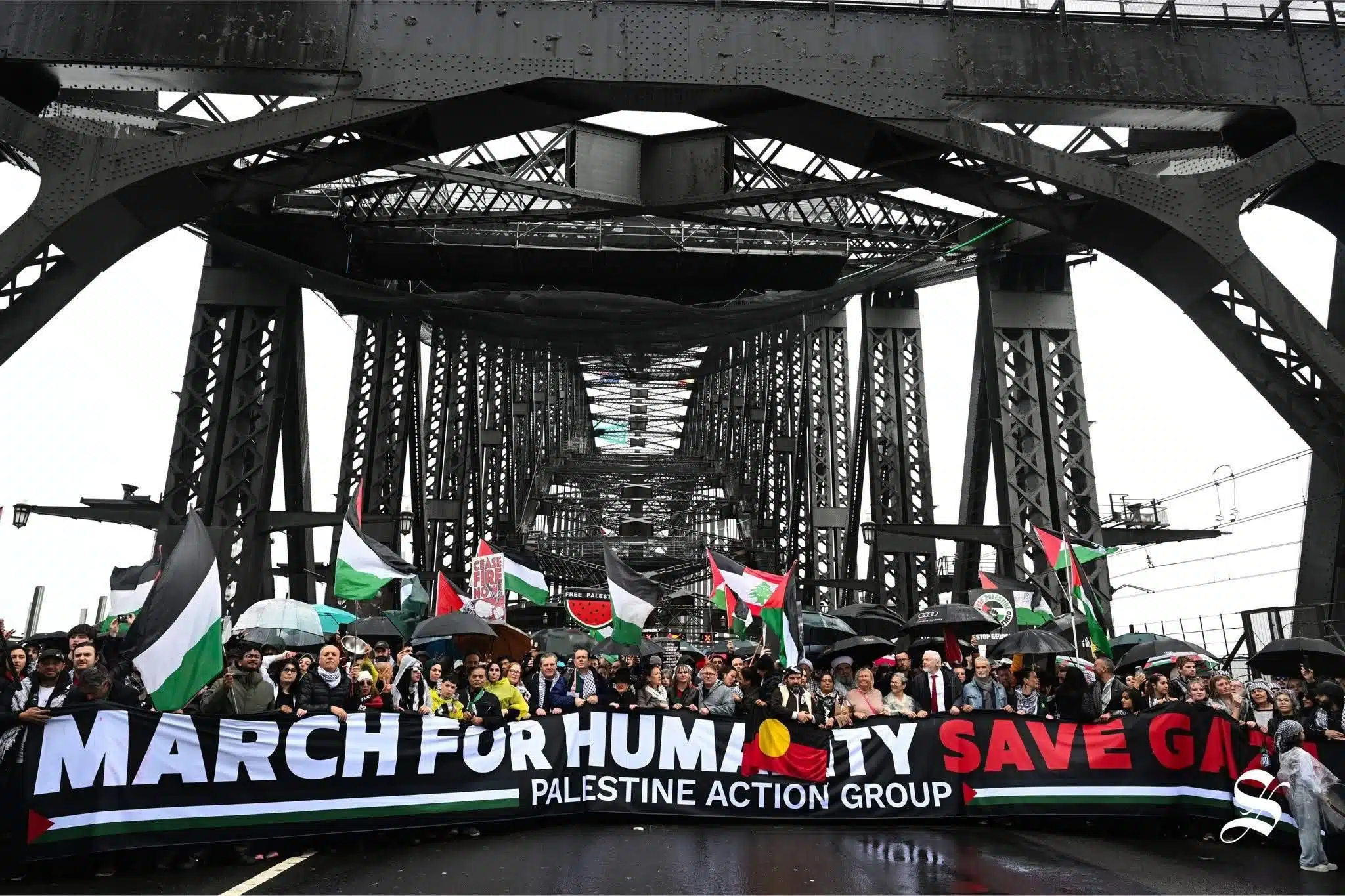 Pro-Palestinian protesters march across Sydney Harbour Bridge holding Palestinian flags and a banner reading “March for Humanity, Save Gaza – Palestine Action Group.”