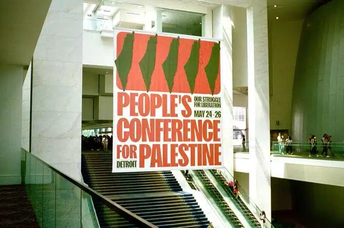 A large banner for the People’s Conference for Palestine hangs inside a Detroit convention center, featuring multiple inverted maps of Israel in red and green.
