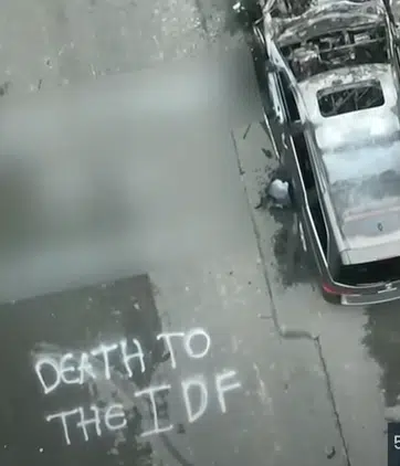 Graffiti reading "Death to the IDF" spray-painted on pavement beside a burned vehicle in a St. Louis residential area.