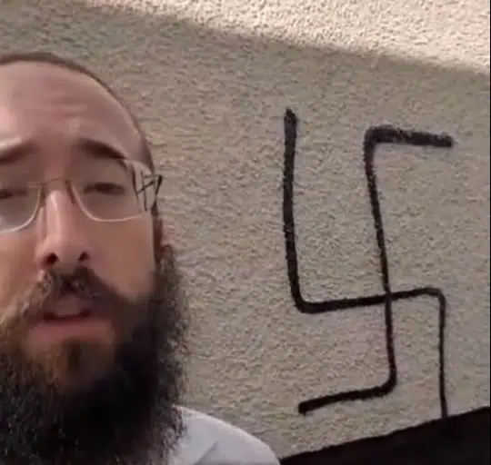Rabbi Bentzion Alperowitz of Chabad Bournemouth stands in front of a Nazi swastika spray-painted on his home.