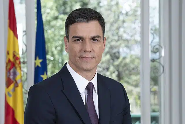 Spanish Prime Minister Pedro Sanchez standing by the Spanish and EU flags.