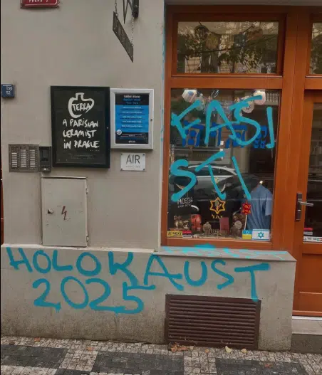 Blue graffiti reading “Fascists” and “Holocaust 2025” are seen spray-painted across the window and wall of a Jewish souvenir and kosher food shop in Prague’s Vinohrady district.