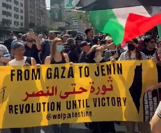 Protesters in New York hold a yellow banner reading “From Gaza to Jenin – Revolution Until Victory” with the full outline of Israel replaced by “Palestine,” alongside Palestinian flags.
