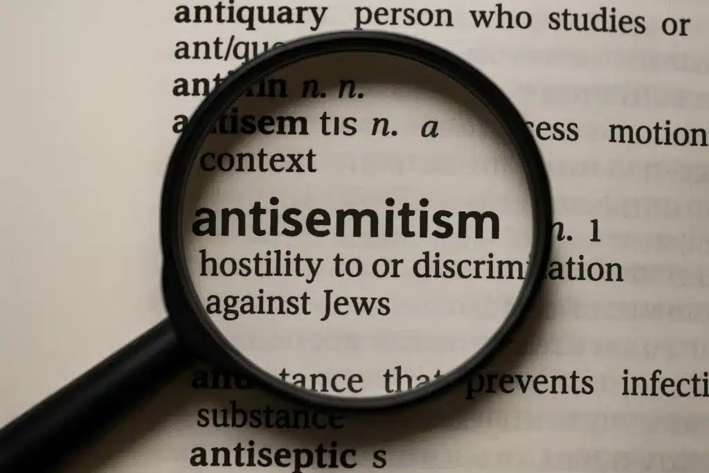 Magnifying glass highlighting the antisemitism definition in a dictionary, showing it as hostility to or discrimination against Jews.