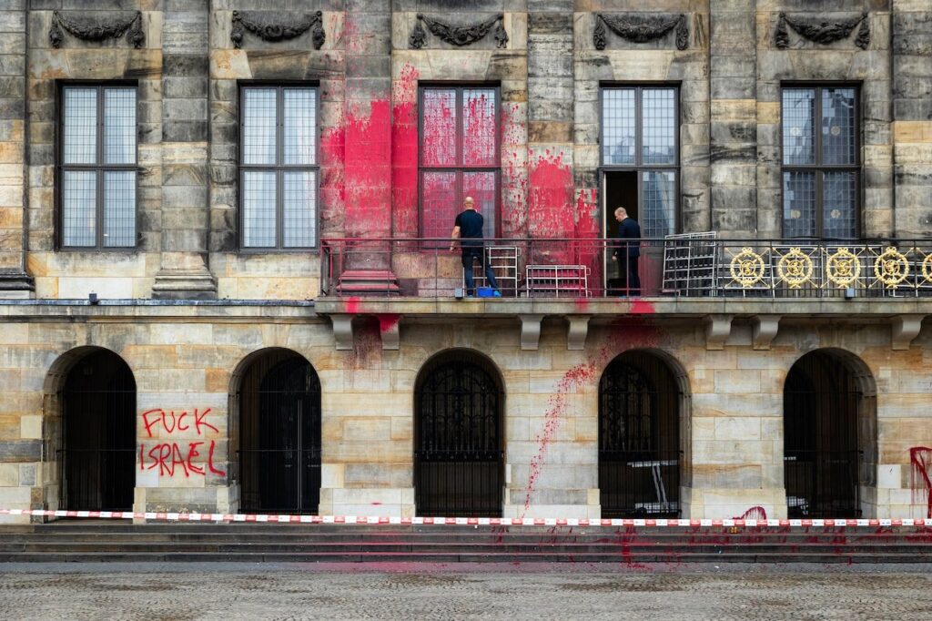 Workers clean red paint splattered across the façade of Amsterdam’s Royal Palace after anti-Israel vandals defaced it with graffiti reading “F*** Israel.”