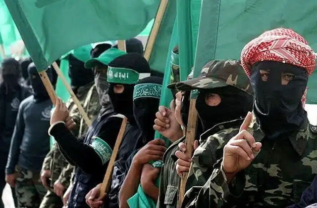 Armed Hamas terrorists wearing camouflage and black masks hold green flags during a public demonstration.