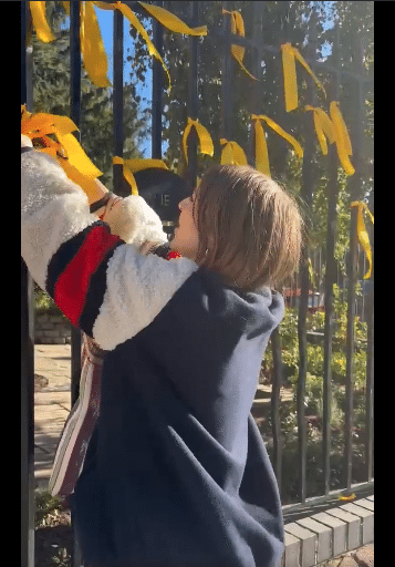Alt text: Woman removes yellow ribbons from a London fence that symbolize solidarity with Israeli hostages held by Hamas.