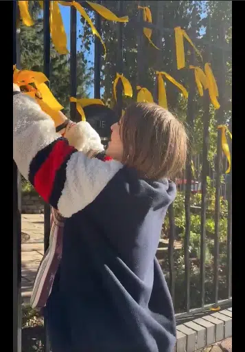 Alt text: Woman removes yellow ribbons from a London fence that symbolize solidarity with Israeli hostages held by Hamas.