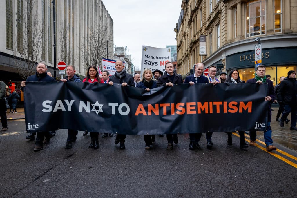 A group of demonstrators march through a city street holding a large banner that reads “Say No to Antisemitism” during an anti-hate rally in the UK.