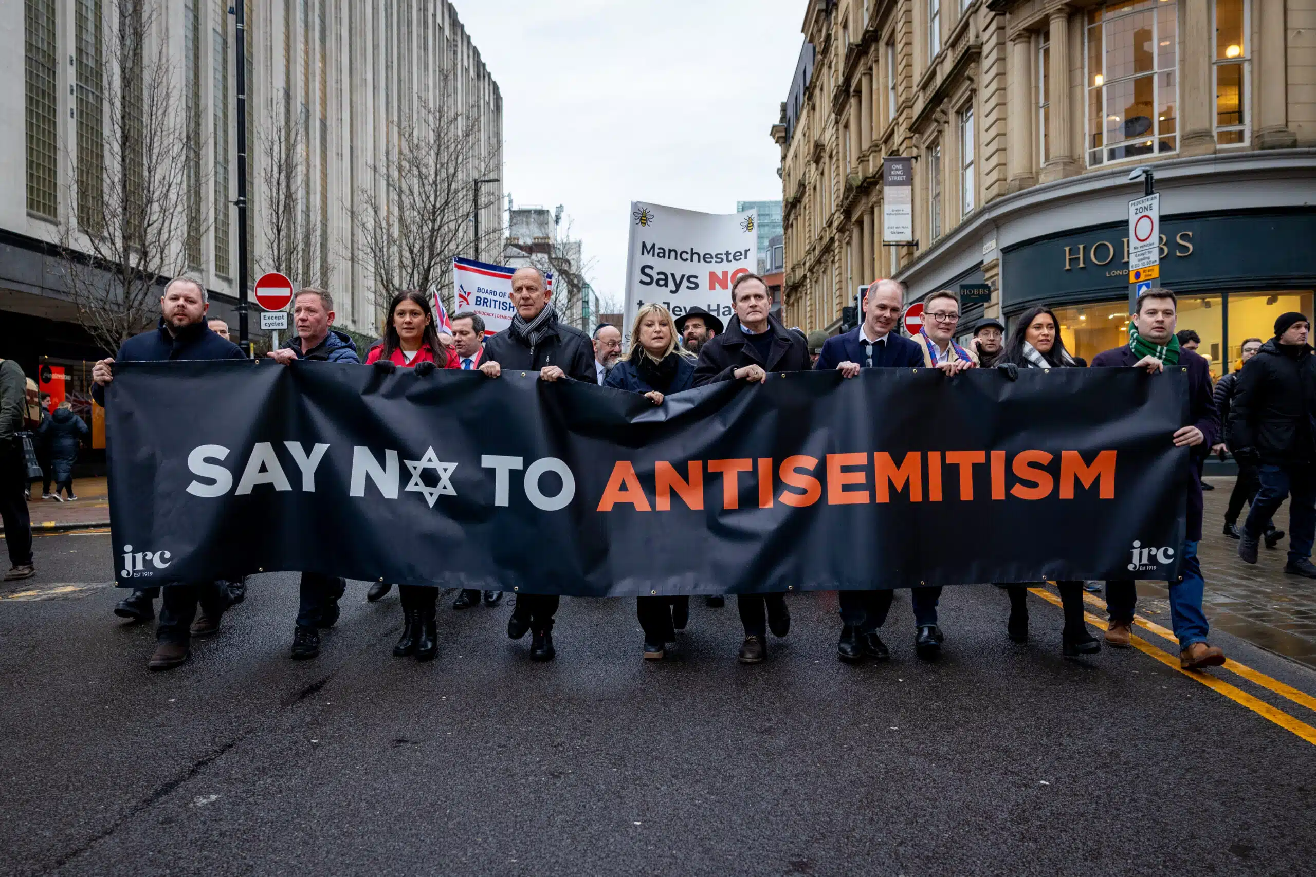 A group of demonstrators march through a city street holding a large banner that reads “Say No to Antisemitism” during an anti-hate rally in the UK.