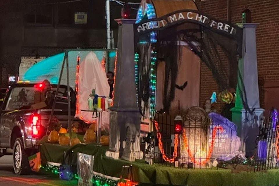 A Halloween parade float designed by St. Joseph Catholic School in Pennsylvania features a replica of the Auschwitz concentration camp gate with the phrase “Arbeit Macht Frei,” illuminated with colored lights and Halloween decorations.