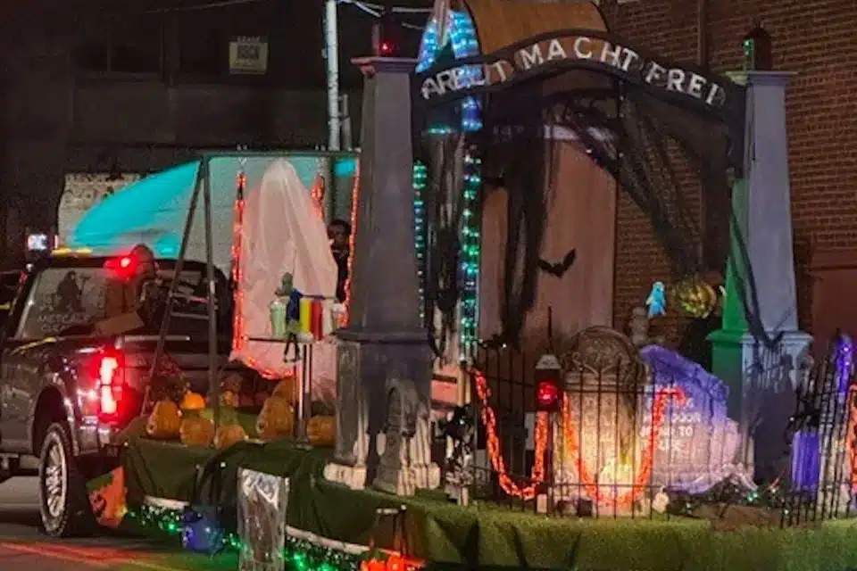 A Halloween parade float designed by St. Joseph Catholic School in Pennsylvania features a replica of the Auschwitz concentration camp gate with the phrase “Arbeit Macht Frei,” illuminated with colored lights and Halloween decorations.