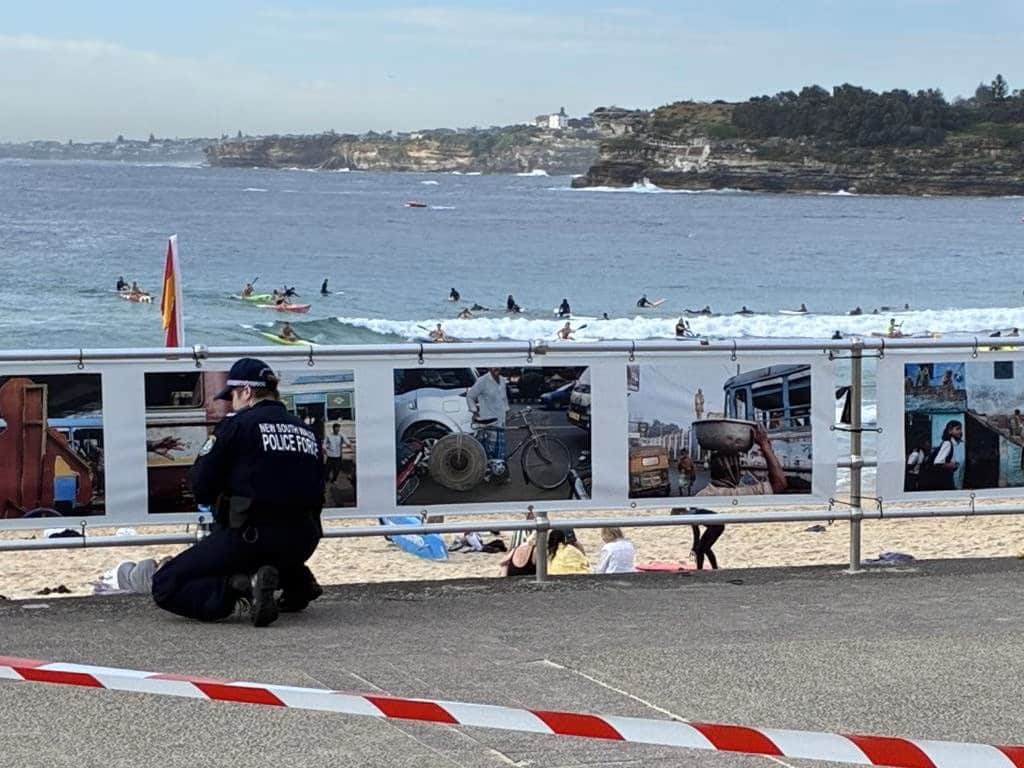 A New South Wales police officer kneels near a taped-off section of Bondi Beach