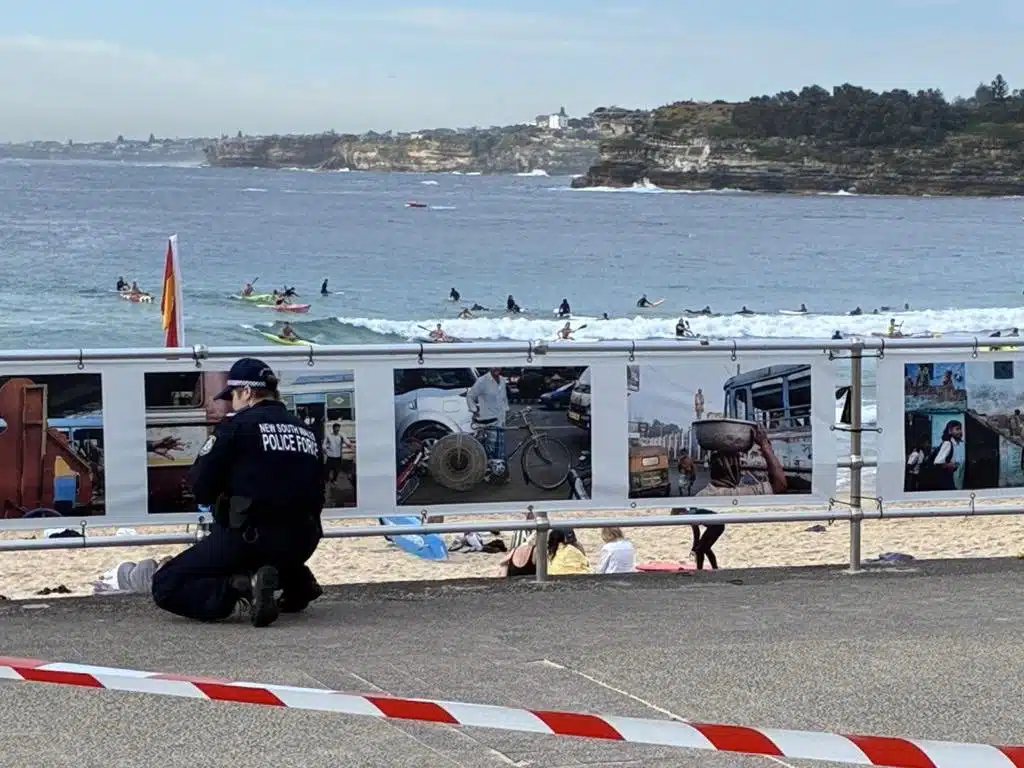A New South Wales police officer kneels near a taped-off section of Bondi Beach