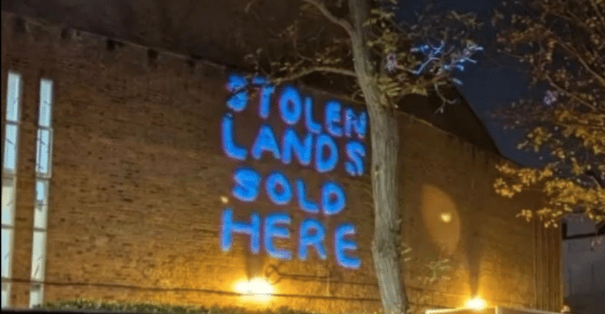Blue light projection reading “Stolen Lands Sold Here” displayed on the exterior wall of St John’s Wood United Synagogue during an anti-Israel protest.