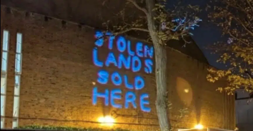 Blue light projection reading “Stolen Lands Sold Here” displayed on the exterior wall of St John’s Wood United Synagogue during an anti-Israel protest.
