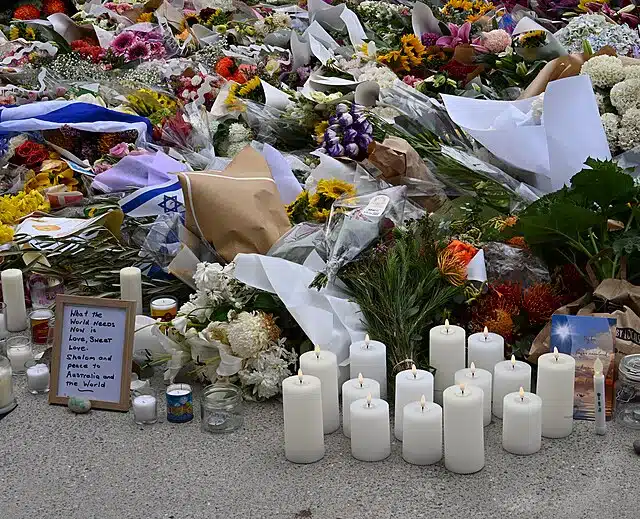 Memorial candles, flowers, and Israeli flags laid at Bondi Beach following the antisemitic attack during a Hanukkah celebration.