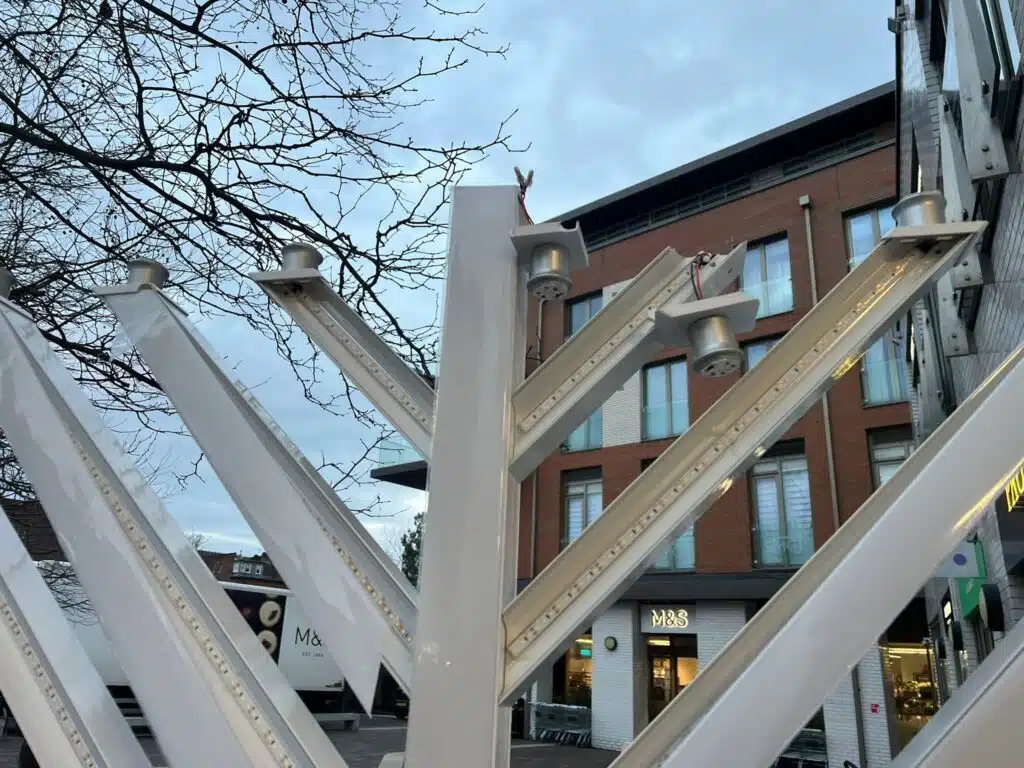 Vandalized public Hanukkah menorah in a London neighborhood, with damaged light fixtures visible against surrounding buildings.