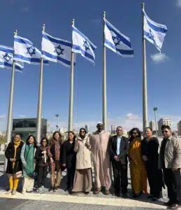 Members of the AMMWEC–CAM delegation stand outside the Knesset in Jerusalem, with Israeli flags visible overhead.