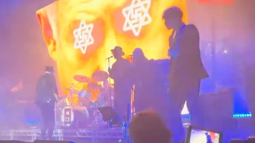 On-stage visuals behind Primal Scream during a London concert display symbols resembling swastikas merged with Stars of David as the band performs.