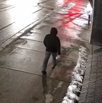 Surveillance image showing a hooded suspect walking near Michigan State University Chabad after antisemitic vandalism involving rock-throwing and swastika graffiti.