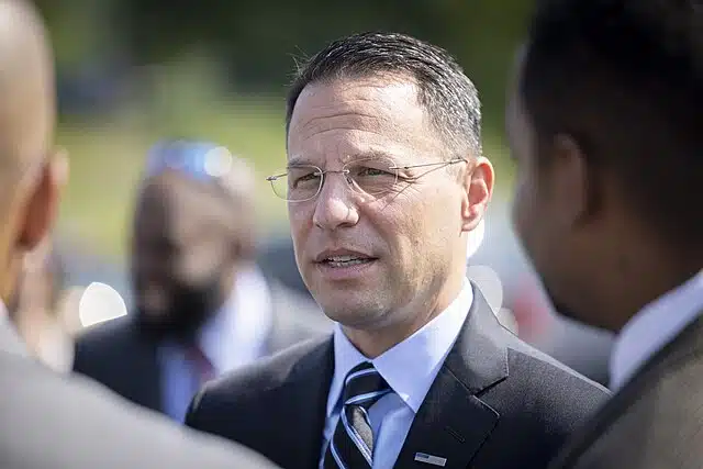 Pennsylvania Governor Josh Shapiro speaks with attendees during an outdoor public event, wearing a dark suit and striped tie.