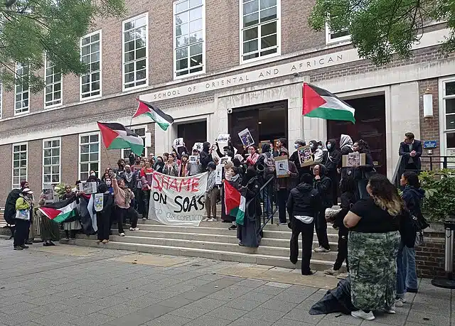 Anti-Israel demonstrators gather outside SOAS University of London, waving Palestinian flags and holding signs during a protest on campus.