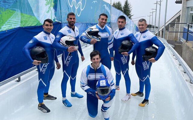 Members of the Israeli national bobsled team pose on an ice track in blue-and-white racing suits, holding helmets ahead of competition in Milan.