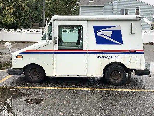 USPS mail truck parked on a residential street in a suburban neighborhood.