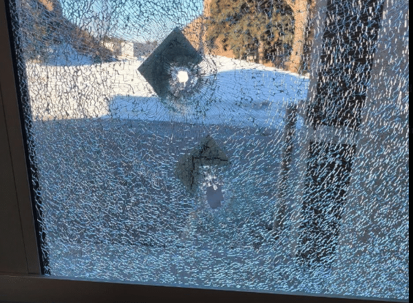 Shattered front window of Toronto’s Temple Emanu-El synagogue showing a bullet hole and spider-web cracking after overnight gunfire damage.