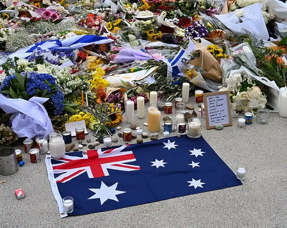 Memorial at Bondi Beach with flowers, candles, and Israeli and Australian symbols honoring victims of the Hanukkah attack.