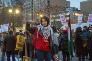 Nerdeen Kiswani, founder of Within Our Lifetime, stands at an anti-Israel protest in New York City surrounded by Palestinian flags and demonstrators holding political signs.