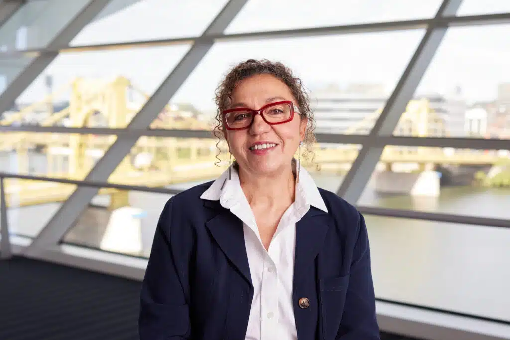 Myrieme Nadri-Churchill, executive director of Parents for Peace, poses for a portrait in front of a large window overlooking a city riverfront.