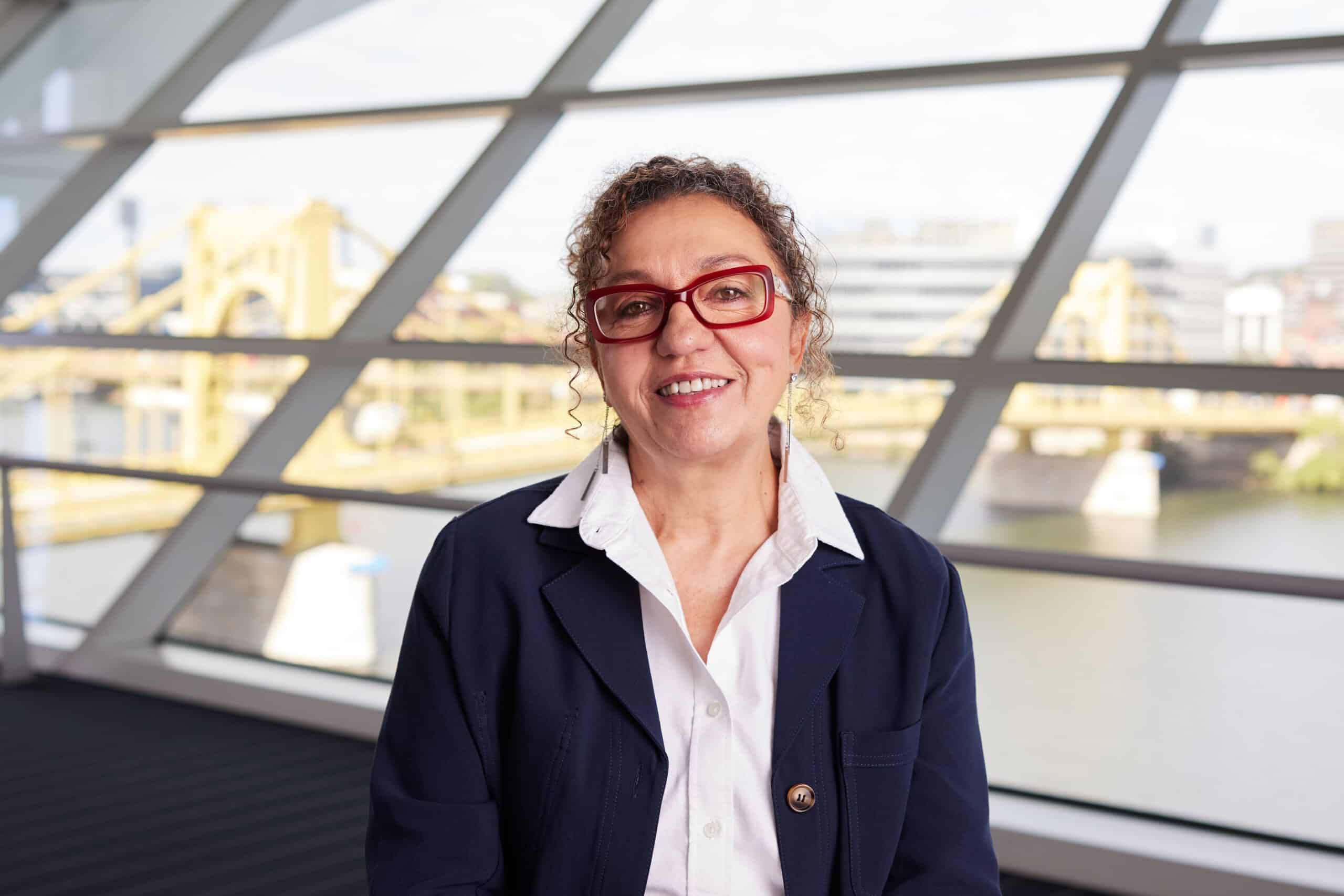 Myrieme Nadri-Churchill, executive director of Parents for Peace, poses for a portrait in front of a large window overlooking a city riverfront.