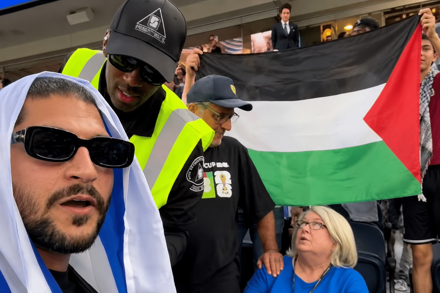 Security personnel confront an Israeli fan at the Iran-New Zealand World Cup match while a Palestinian flag remains visible in the stands behind them.