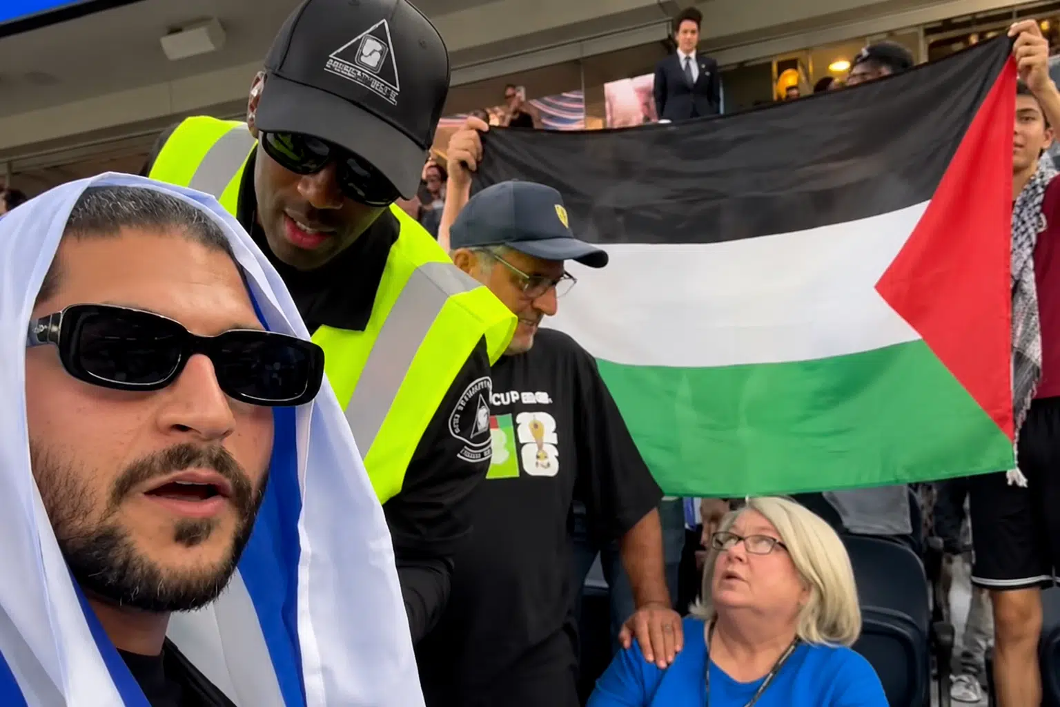 Security personnel confront an Israeli fan at the Iran-New Zealand World Cup match while a Palestinian flag remains visible in the stands behind them.