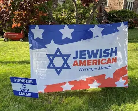 Jewish American Heritage Month flag displayed on a lawn beside a sign reading “Standing With Israel.”