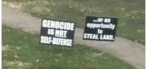 Two lawn signs displayed on a residential property reading "Genocide Is Not Self-Defense" and "...or an opportunity to steal land."