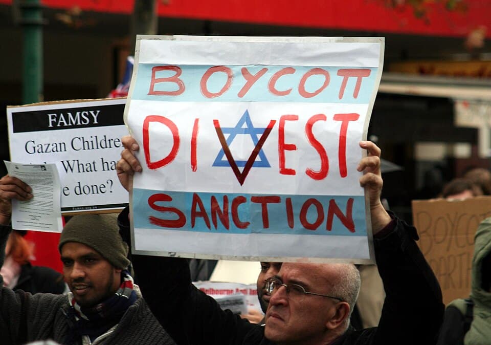 A protester holds a "Boycott, Divest, Sanction" (BDS) sign featuring an Israeli flag during a pro-Palestinian demonstration.