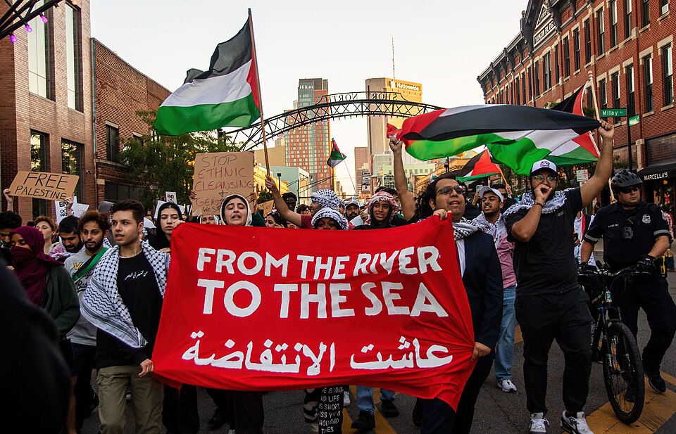 Demonstrators hold Palestinian flags and a red banner reading “From the river to the sea.”
