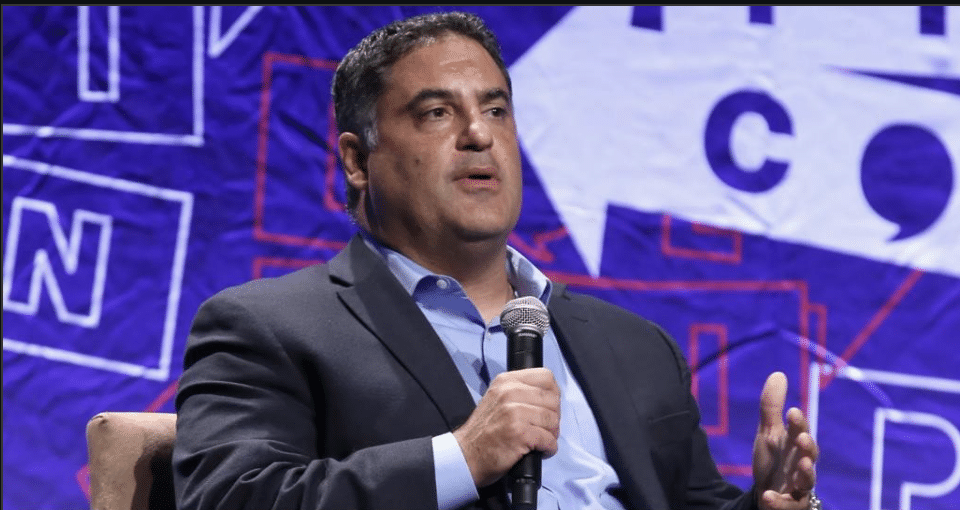 Cenk Uygur speaks into a handheld microphone during an onstage discussion.