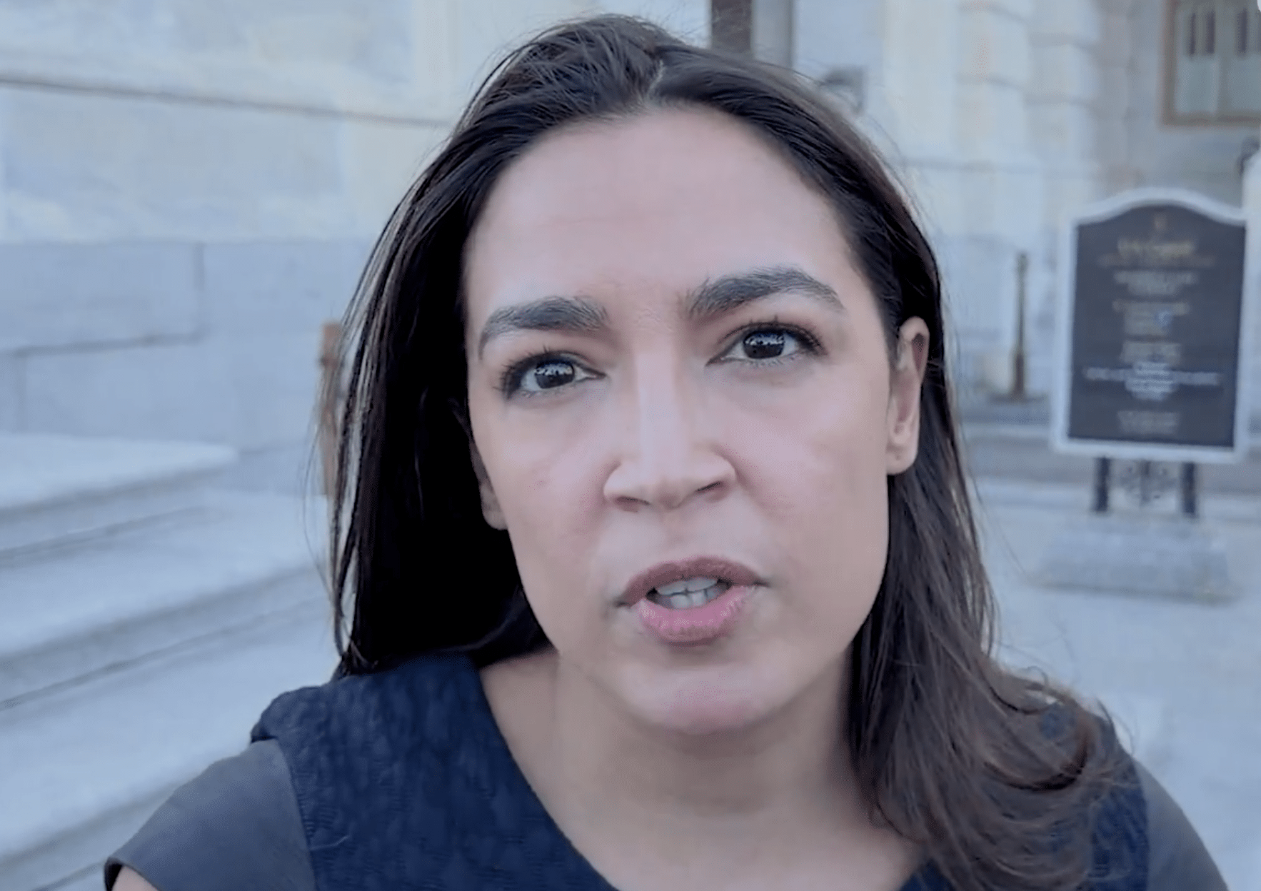 Rep. Alexandria Ocasio-Cortez speaking outdoors in front of a stone building.